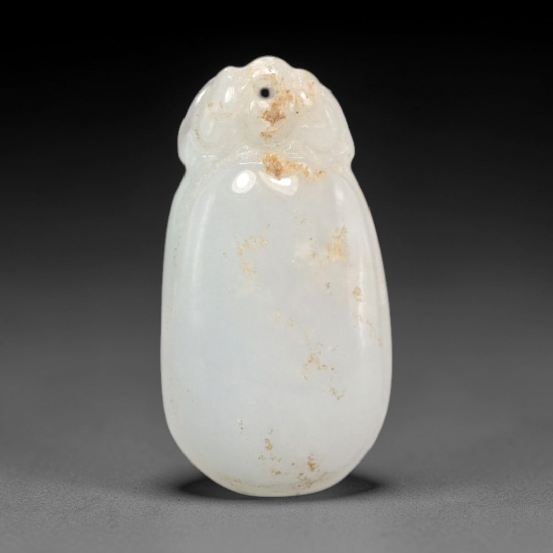 A Chinese Jadeite Jade Pendant, 20th Century, 58FR: Carved from translucent white jadeite jade with natural brownish inclusions and tonal variations, the pendant has an oval form with a raised, stylized double-loop bail at the apex, which features a dr