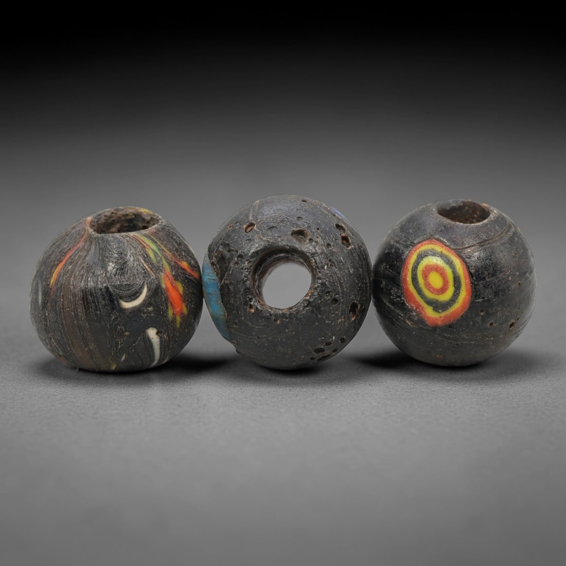 A Group of Venetian Mosaic and Swirl Glass Beads, 19th-20th Century, 89ZM: Fabricated from opaque and translucent glass, the group consists of three spherical beads with central perforations for suspension. One bead displays a black base with swirling red, green, yellow, and