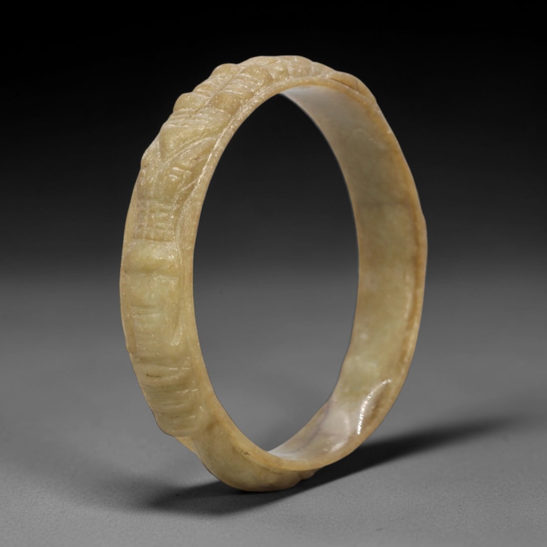 A Chinese Jadeite Jade Bangle Bracelet, 20th Century, 31FS: Carved from pale yellowish-green jadeite jade with natural tonal variation and subtle surface texture, the bangle is formed as a continuous circular band. The exterior surface is decorated with raised