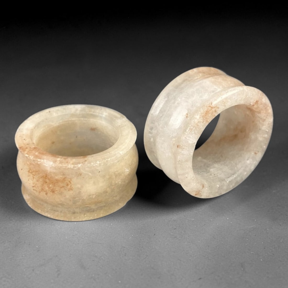 A Pair of Chinese Quartz Archer Rings - 20th Century, 57FX: Crafted from translucent milky quartz with natural russet mineral inclusions, this pair of archer rings features hollow cylindrical forms with raised collars at both ends, consistent with traditional