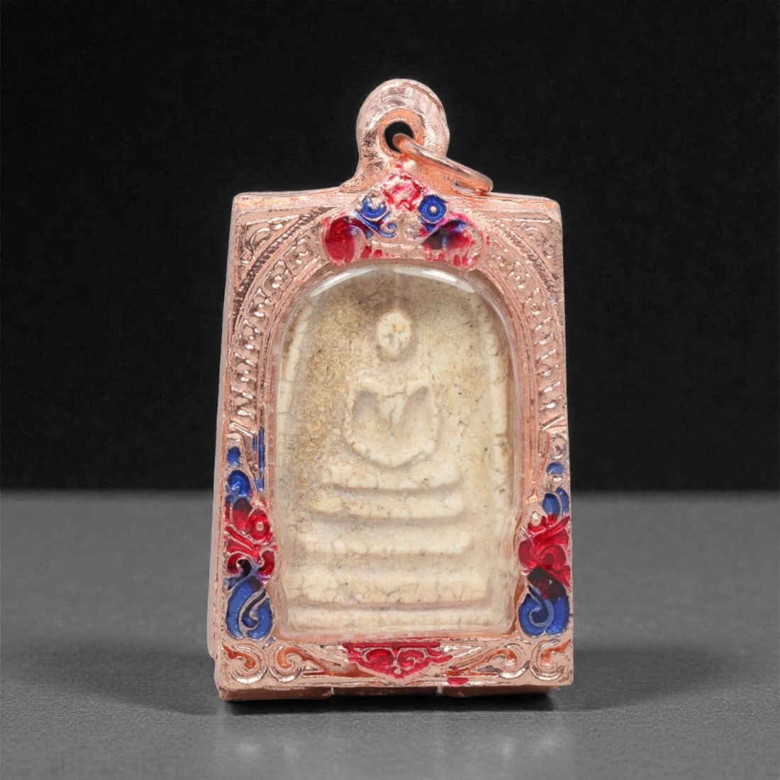 A Thai Phra Somdej Amulet Pendant, 20th Century, 13FP: This rectangular pendant features a traditional Phra Somdej core, encased in a copper frame with a transparent protective cover, measuring 3 x 5.6 cm (1 3/16 x 2 3/16 in.). The obverse displays the ic