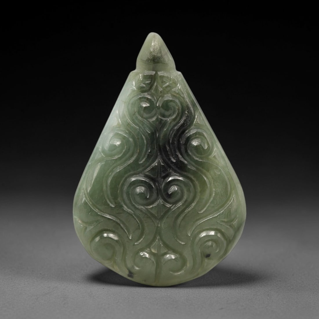 A Chinese Jadeite Jade Scrollwork Pendant, 20th Century, 86FR: Carved from variegated pale green and dark green jadeite jade with natural tonal variations, the pendant has a teardrop-shaped form with a raised, pointed apex. The entire surface is decorated with sy