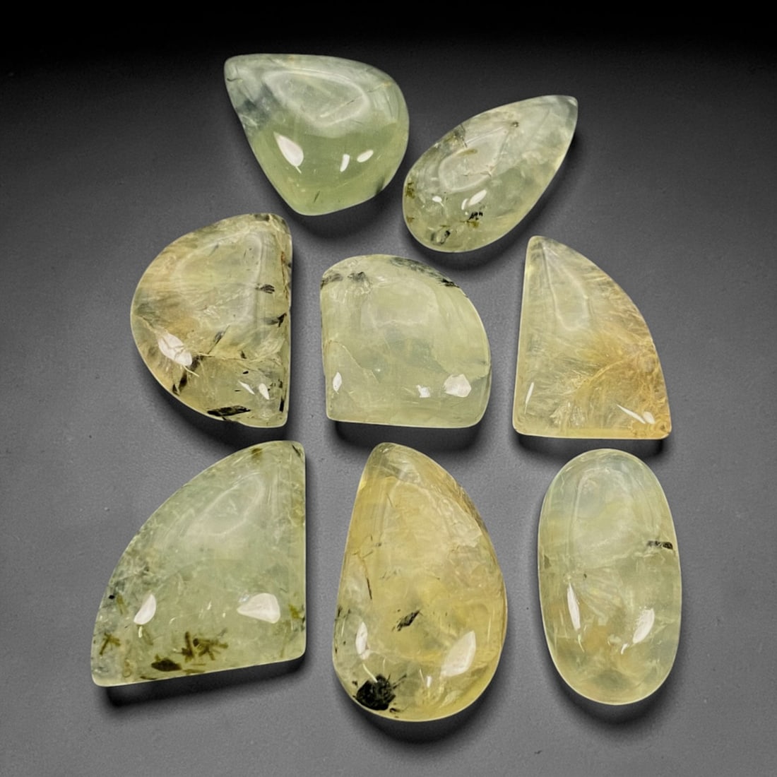 219 Carats Prehnite Cabochon Suite - Natural Malagasy Single Parcel, 68ZJ: This substantial suite of eight prehnite cabochons, ranging in size from 2.1 to 3.1cm, features a palette of soft, translucent green to pale yellow-green hues, characteristic of high-quality prehnite