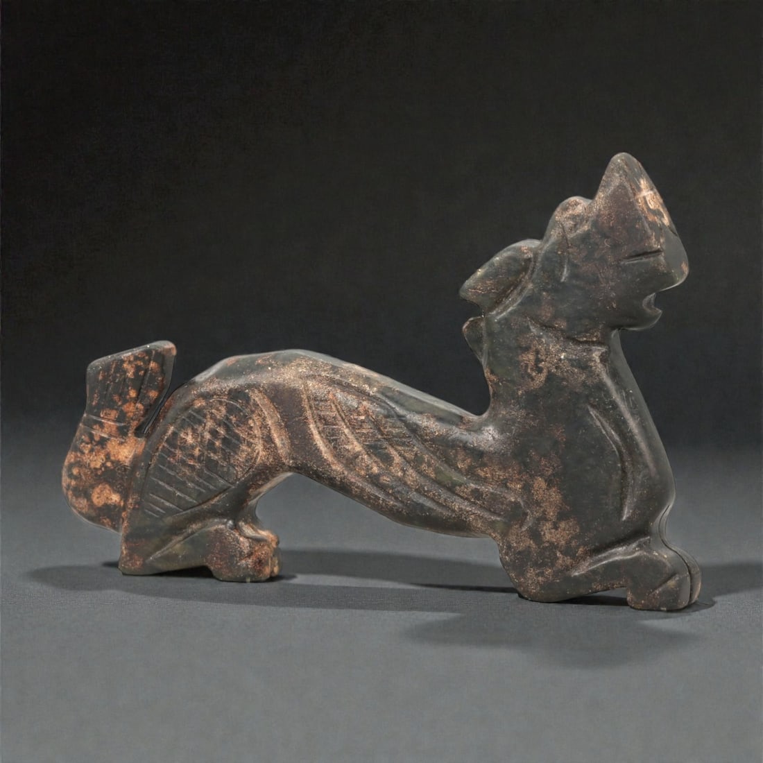 A Chinese Nephrite Jade Dragon Figure, 20th Century, 82FB: Carved from dark green to nearly black nephrite jade with extensive brown surface accretions and mineral inclusions, the figure is modeled as an elongated dragon shown in a striding, arched posture. T