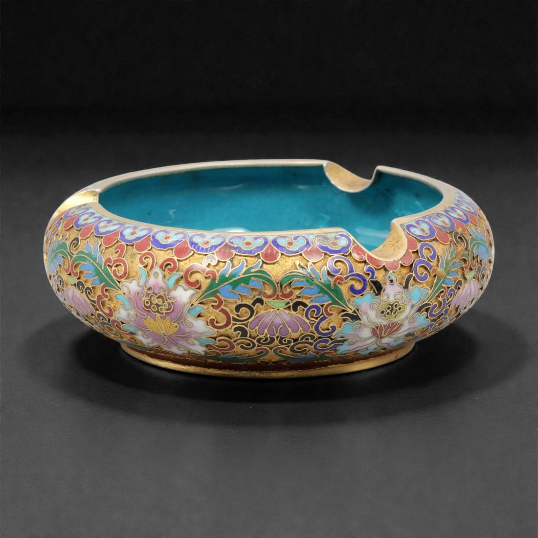 A Chinese Cloisonne Enamel Ashtray, 20th Century, 89YC: Formed as a shallow circular vessel with a broad rim and three evenly spaced notches for cigarette rests, the ashtray is constructed over a metal core and decorated externally in cloisonne enamel on a