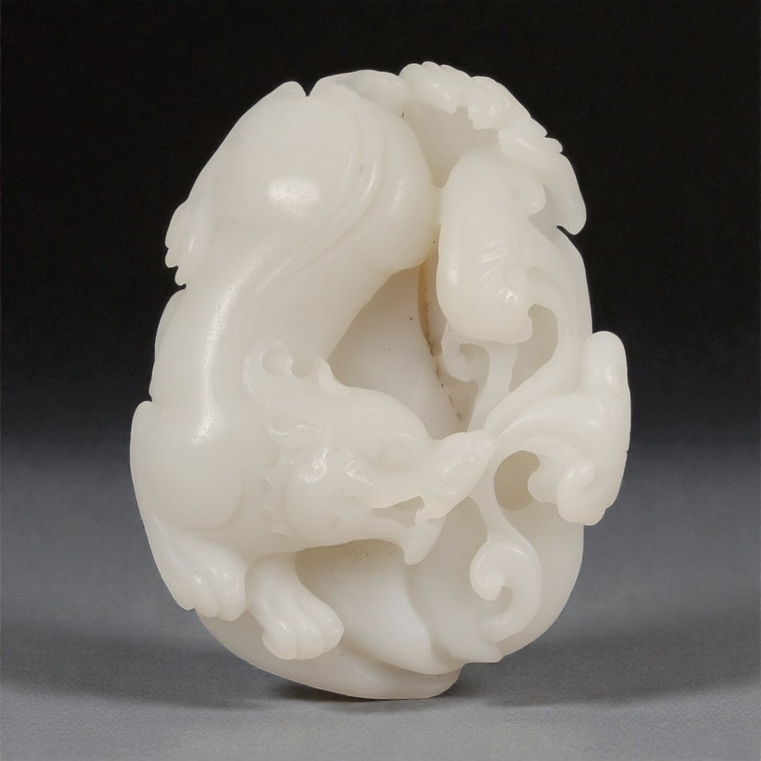 A Chinese Hetian Jade Carving of a Mythical Beast, 20th Century, 7FD: Carved from pale white Hetian jade with a soft, even translucency, the object is worked as a compact openwork carving depicting a stylized mythical beast. The creature is rendered in a dynamic crouchi