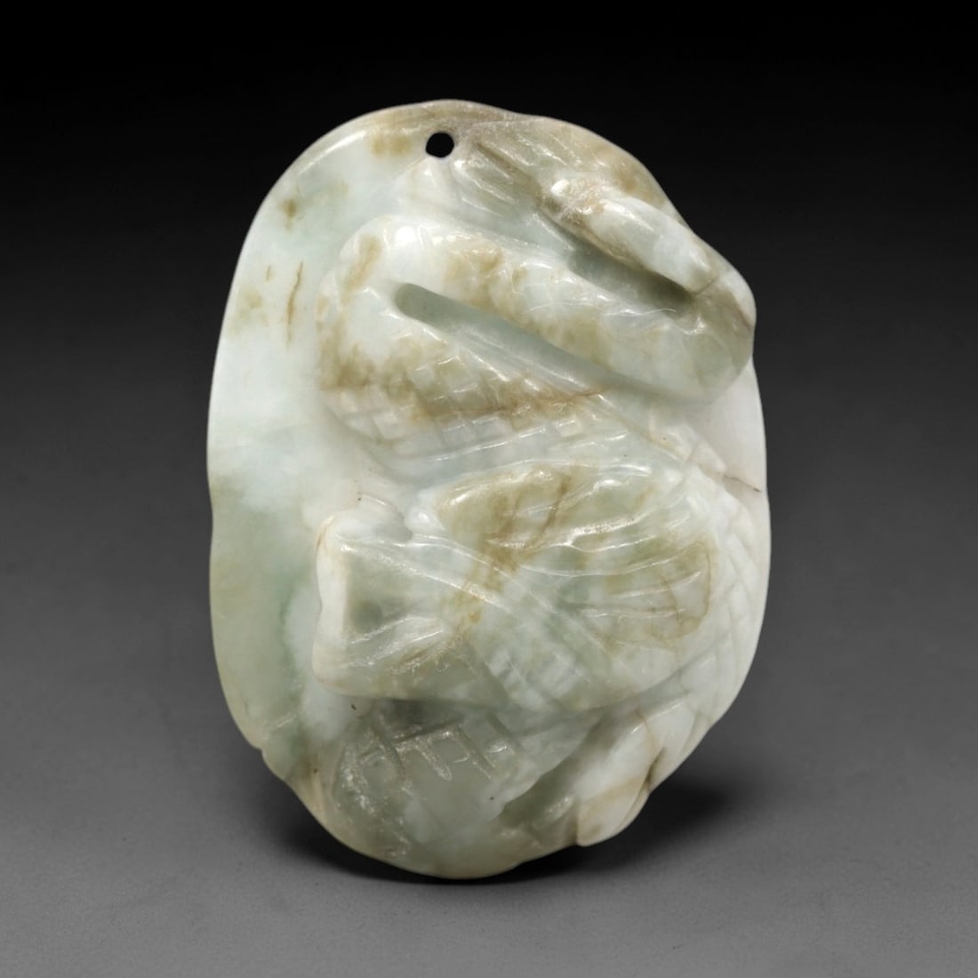 A Chinese Jadeite Jade Dragon-Form Pendant Plaque, 20th Century, 35FR: Carved from pale greenish-white jadeite jade with prominent brownish inclusions and subtle internal veining, the pendant is formed as an irregularly shaped, flattened plaque. The surface is executed i