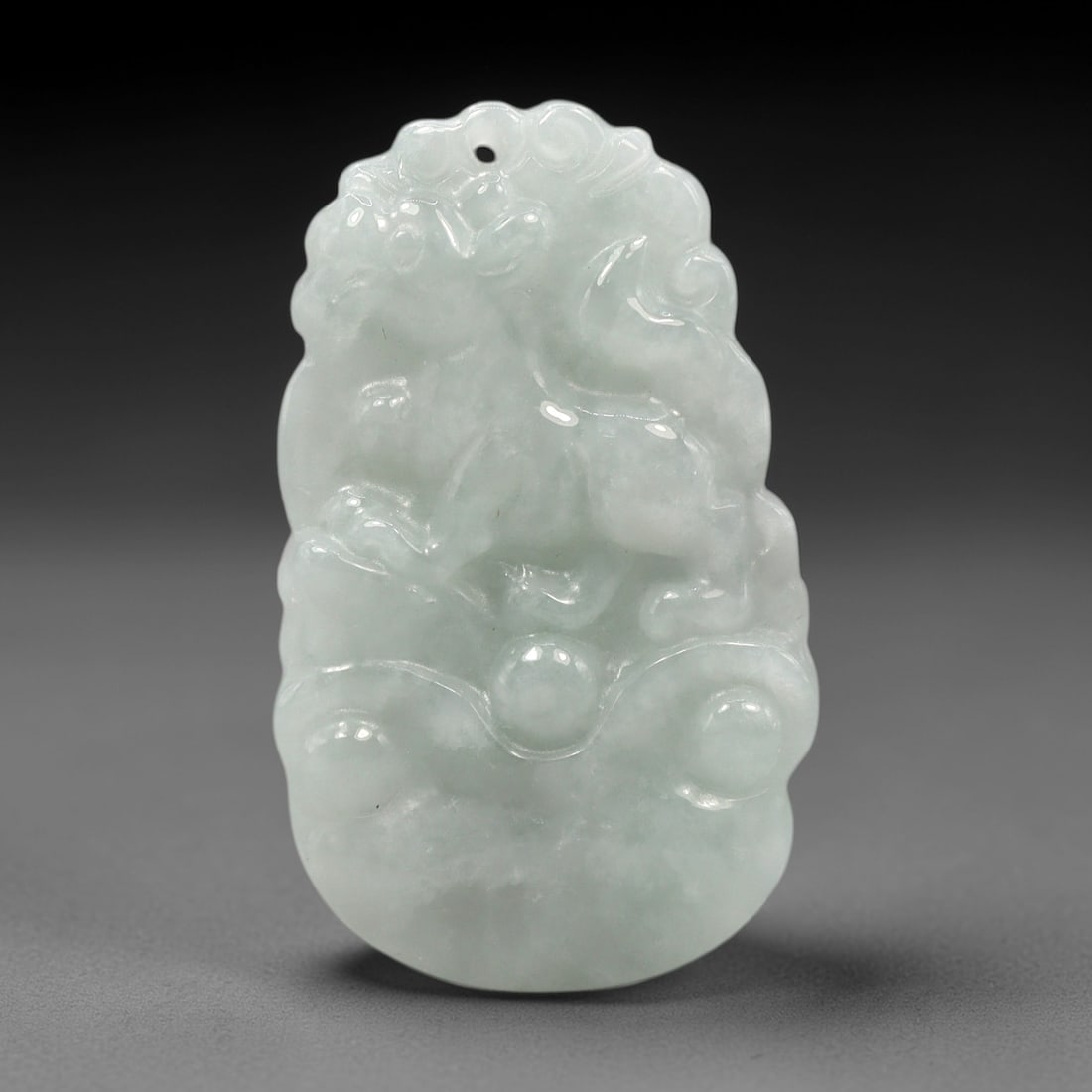 A Chinese Jadeite Jade Dog Pendant, 20th Century, 99XL: Carved from pale green jadeite with subtle tonal variation and minor natural inclusions, the pendant is shaped in an irregular, slightly elongated form with a central suspension hole at the top. The s