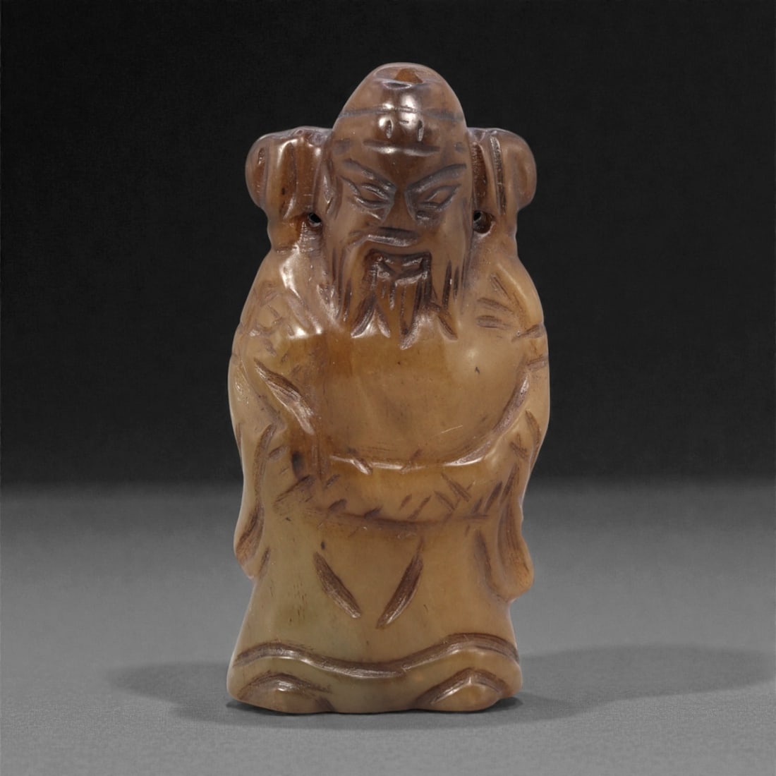 A Chinese Hetian Jade Figure, 20th Century, 86FH: Carved from Hetian jade with warm honey-brown and pale beige tonal variation, the figure is worked in the round and stands upright on a gently flattened base. The subject is shown wearing long robes w