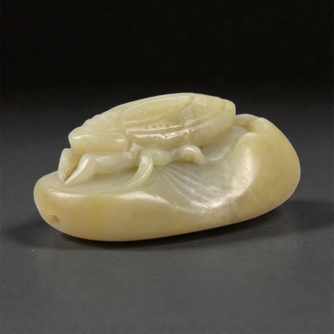A Chinese Jade Cicada Carving, 20th Century, 5FB: Carved from pale yellow jade with a creamy, semi-translucent appearance and scattered natural inclusions, the object represents a cicada carved in relief against an oval ground. The insect is shown fr