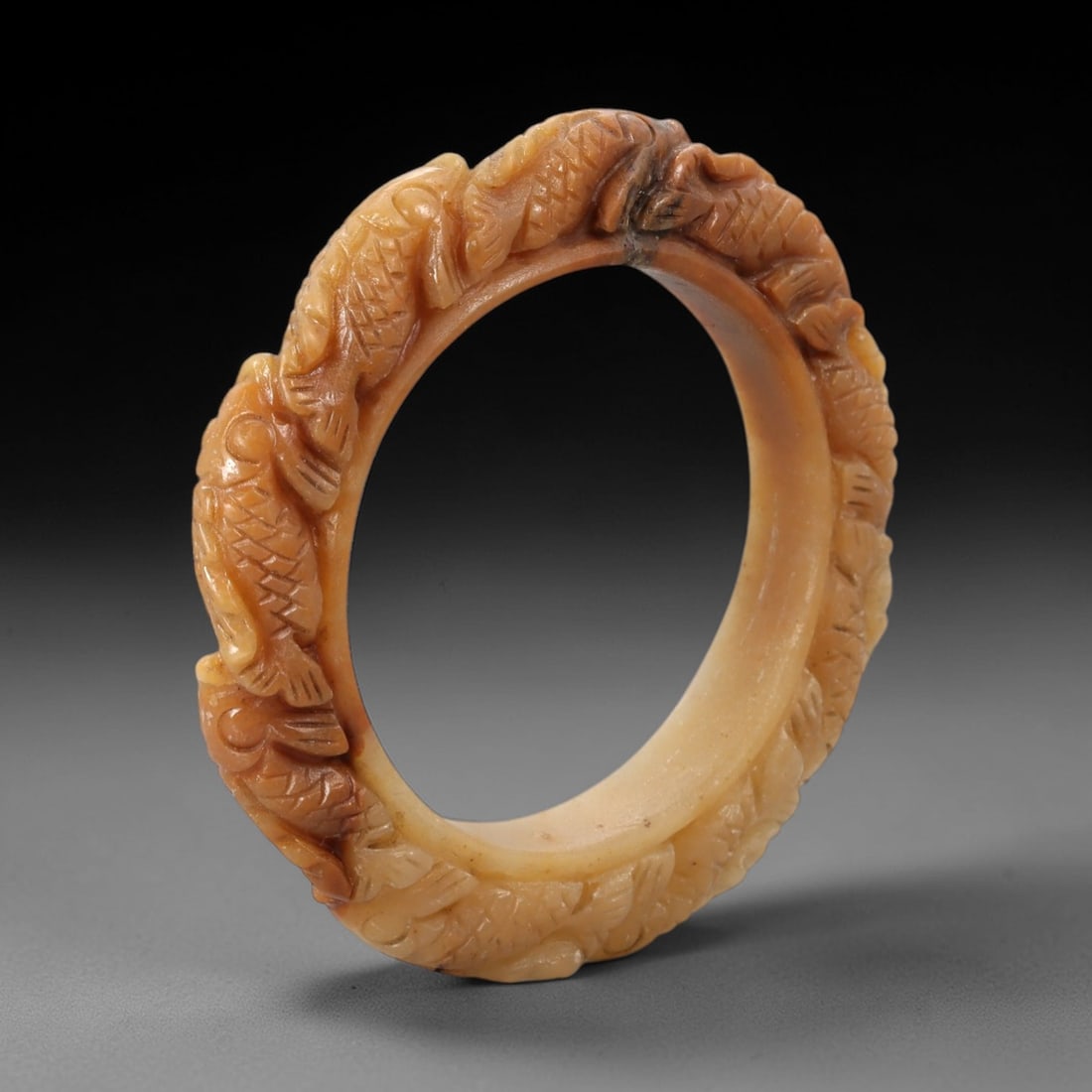 A Chinese Carved Jadeite Jade Bangle Bracelet, 20th Century, 66ZL: A fine jadeite bangle of flattened circular form, masterfully carved in high relief with a continuous band of stylized carp motifs. The stone exhibits a rich, variegated palette, with a creamy white b
