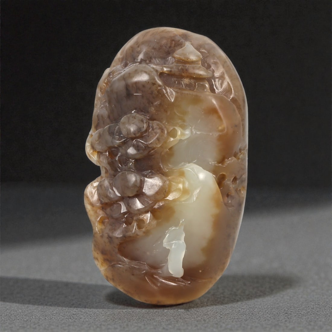 A Chinese Hetian Jade Lingzhi and Rockwork Relief Plaque, 20th Century, 35YA: Carved from mottled Hetian jade with natural areas of creamy white, warm brown, and pale caramel coloration, the plaque is worked in relief on one face to take advantage of the stone's variegated tone