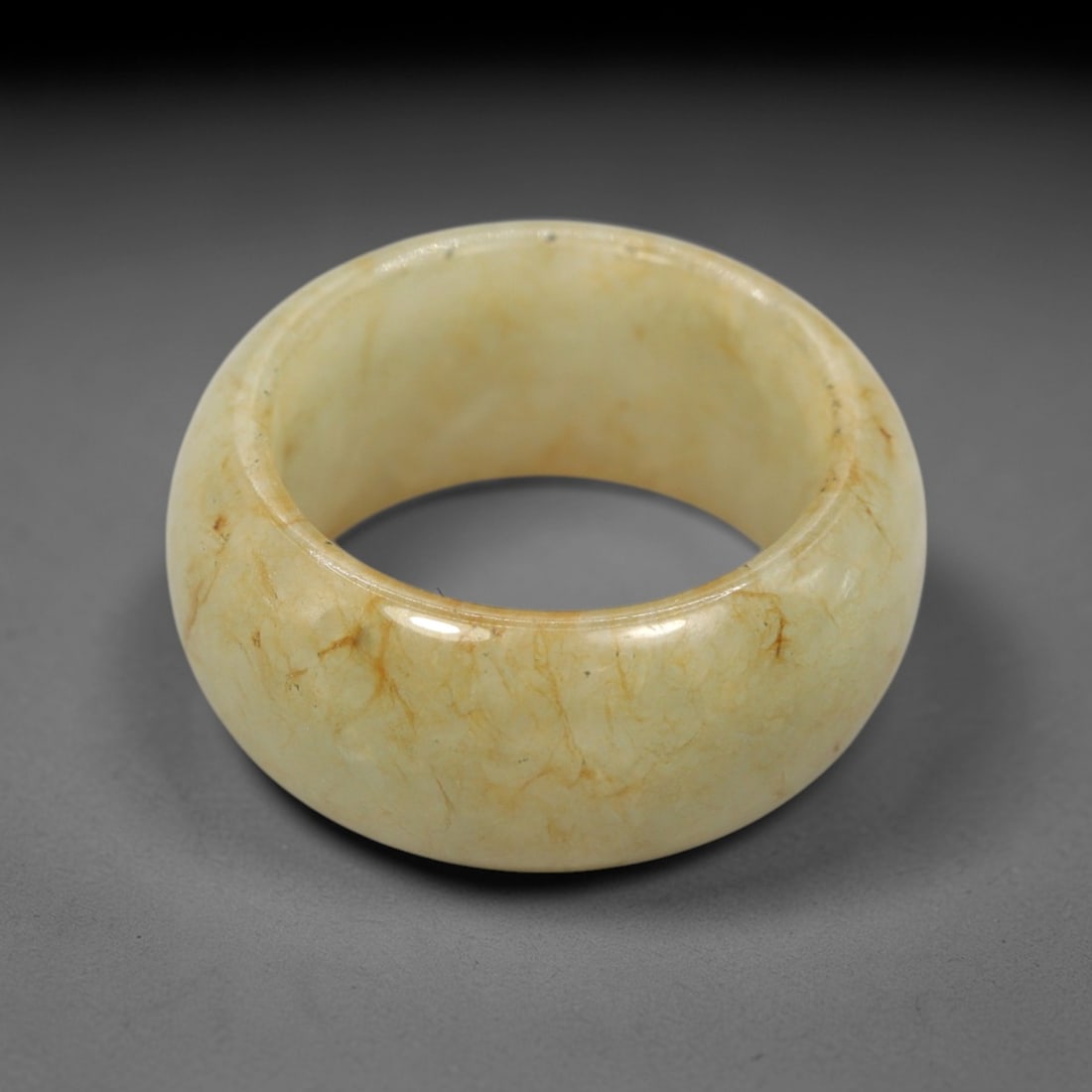 A Chinese Nephrite Jade Ring, 20th Century, 71FT: Carved from pale yellowish nephrite jade with prominent natural golden-brown veining and inclusions distributed throughout the matrix, the ring is formed as a thick, circular band with a smooth, highl