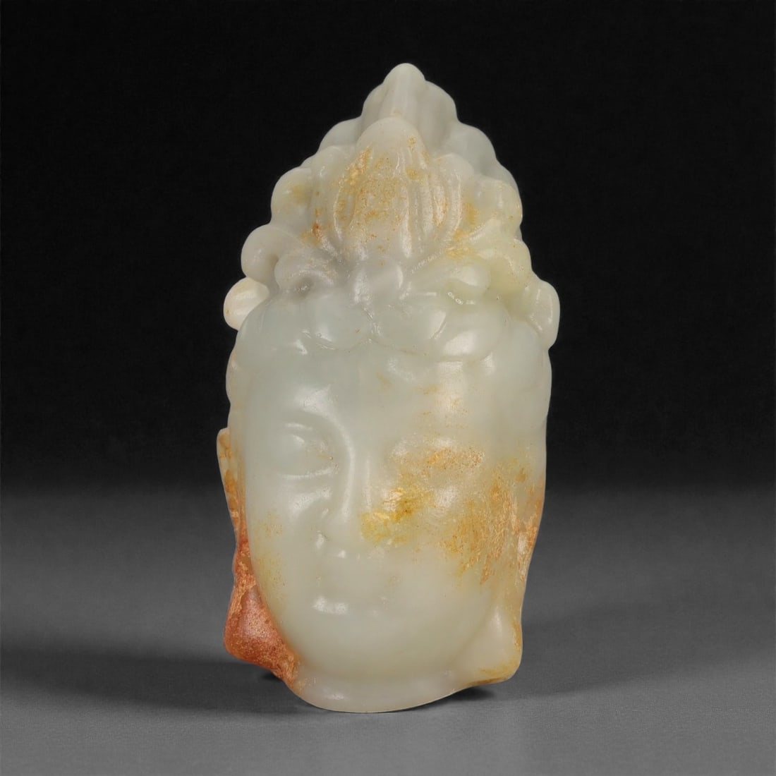 A Chinese Hetian Nephrite Jade Buddha Head, 20th Century, 51FD: Carved from pale celadon Hetian nephrite jade with areas of natural translucency and retained russet skin along the sides and rear. The sculpture represents the head of a Buddha, modeled with a rounde