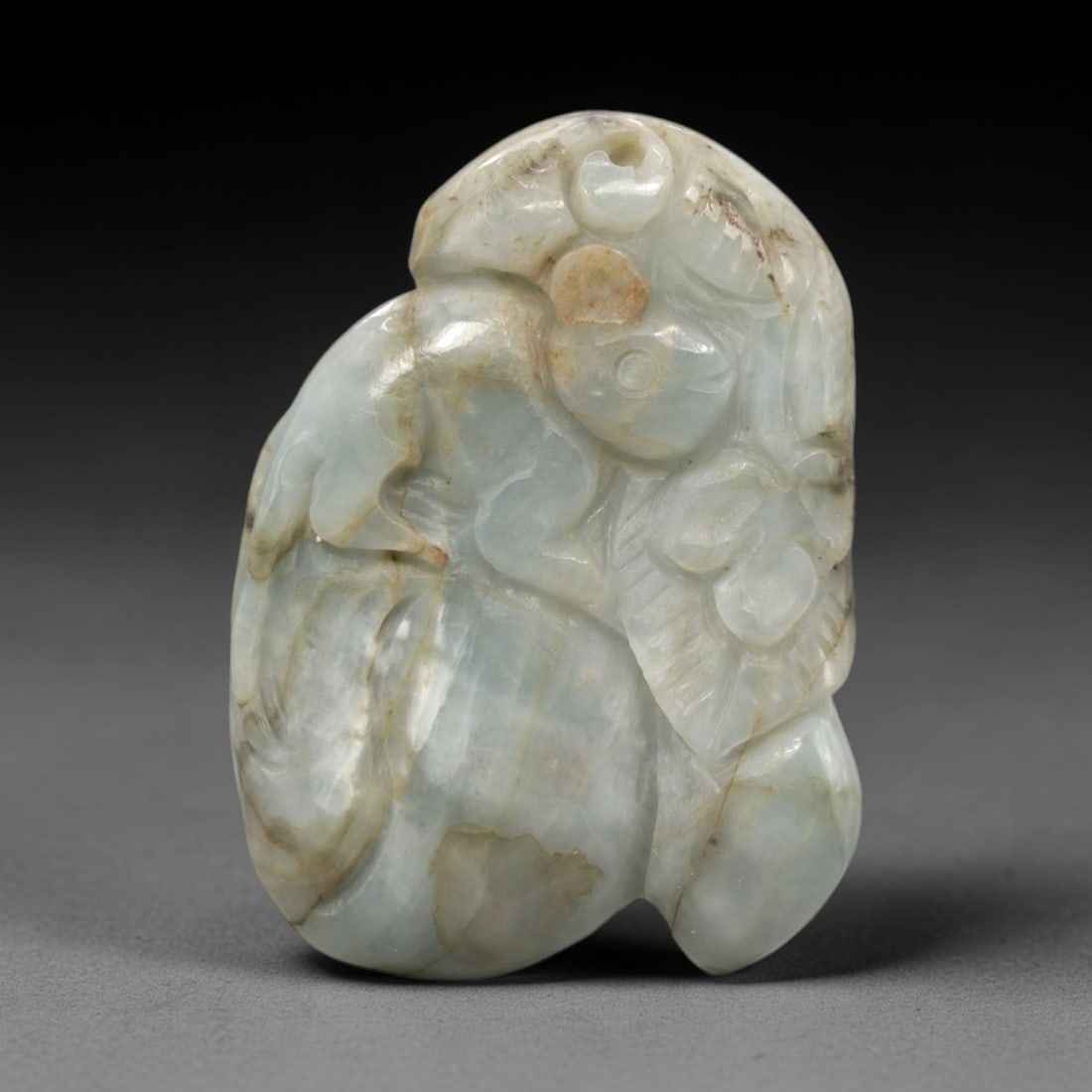 A Chinese Jadeite Jade Monkey and Peach Pendant, 20th Century, 72FR: Carved from pale greenish-white jadeite jade with natural tonal variation and scattered brown mineral inclusions, the pendant is executed in relief. A monkey is depicted atop a peach, with the creatur