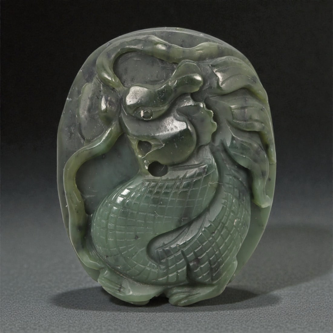 A Chinese Nephrite Jade Dragon Relief Plaque, 20th Century, 15YA: Carved from dark green nephrite jade with areas of lighter translucency and scattered natural inclusions, the plaque is worked in relief on one face with a coiled dragon shown in a compact, vertical c