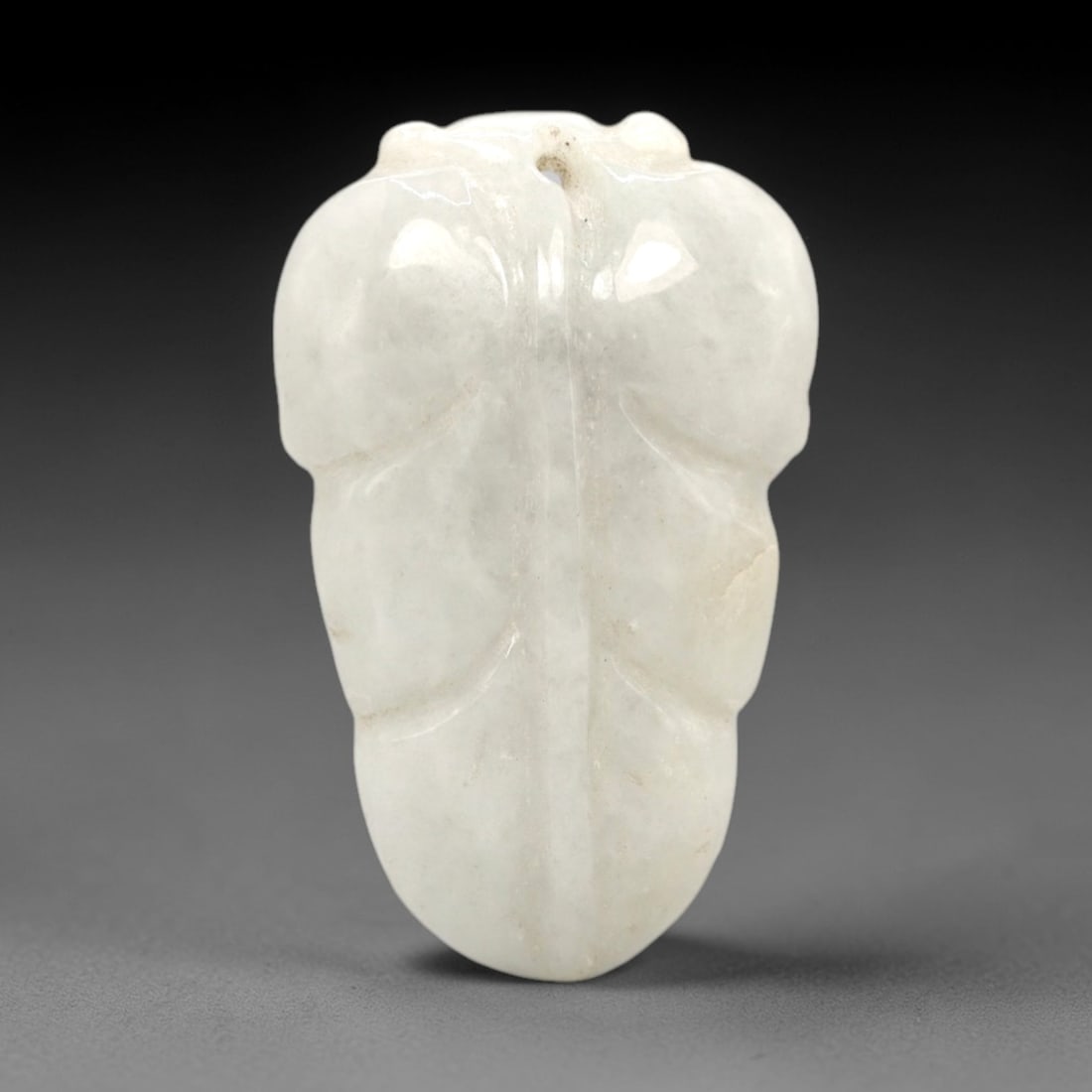 A Chinese Jadeite Jade Leaf-Form Pendant, 20th Century, 77FR: Carved from opaque white jadeite jade with subtle natural granular inclusions, the pendant is shaped in the form of a stylized double leaf. A central vertical raised ridge divides the two lobes, with