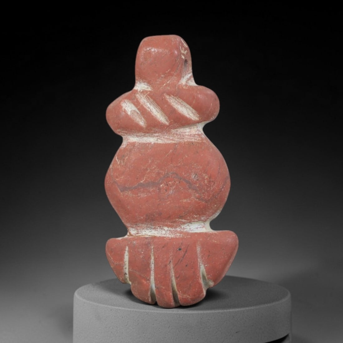 Ancient Stone Anthropomorphic Amulet - Near Eastern Figurine, 33AP: Carved from a rich, reddish stone with natural mineral inclusions and weathered patina, this amulet depicts a stylized anthropomorphic form with a simplified, rounded head, bulbous torso, and fan-shap