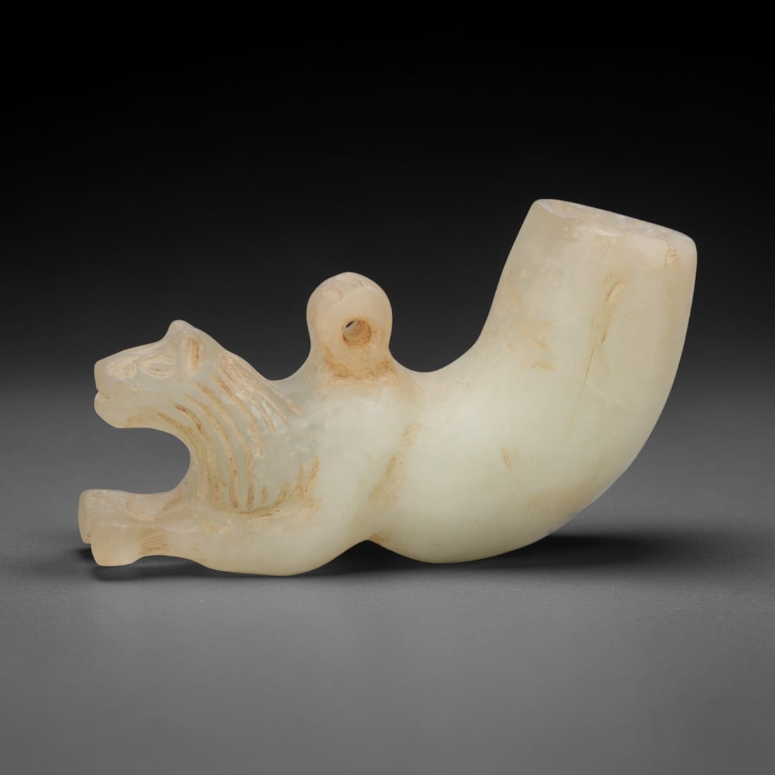 Ancient Marble Rhyton Amulet - Animal Form Figurine, 97XR: Crafted from pale marble, this object takes the form of a rhyton-shaped amulet, with a stylized animal figure integrated into its curved body. The animal head, rendered with incised linear details def