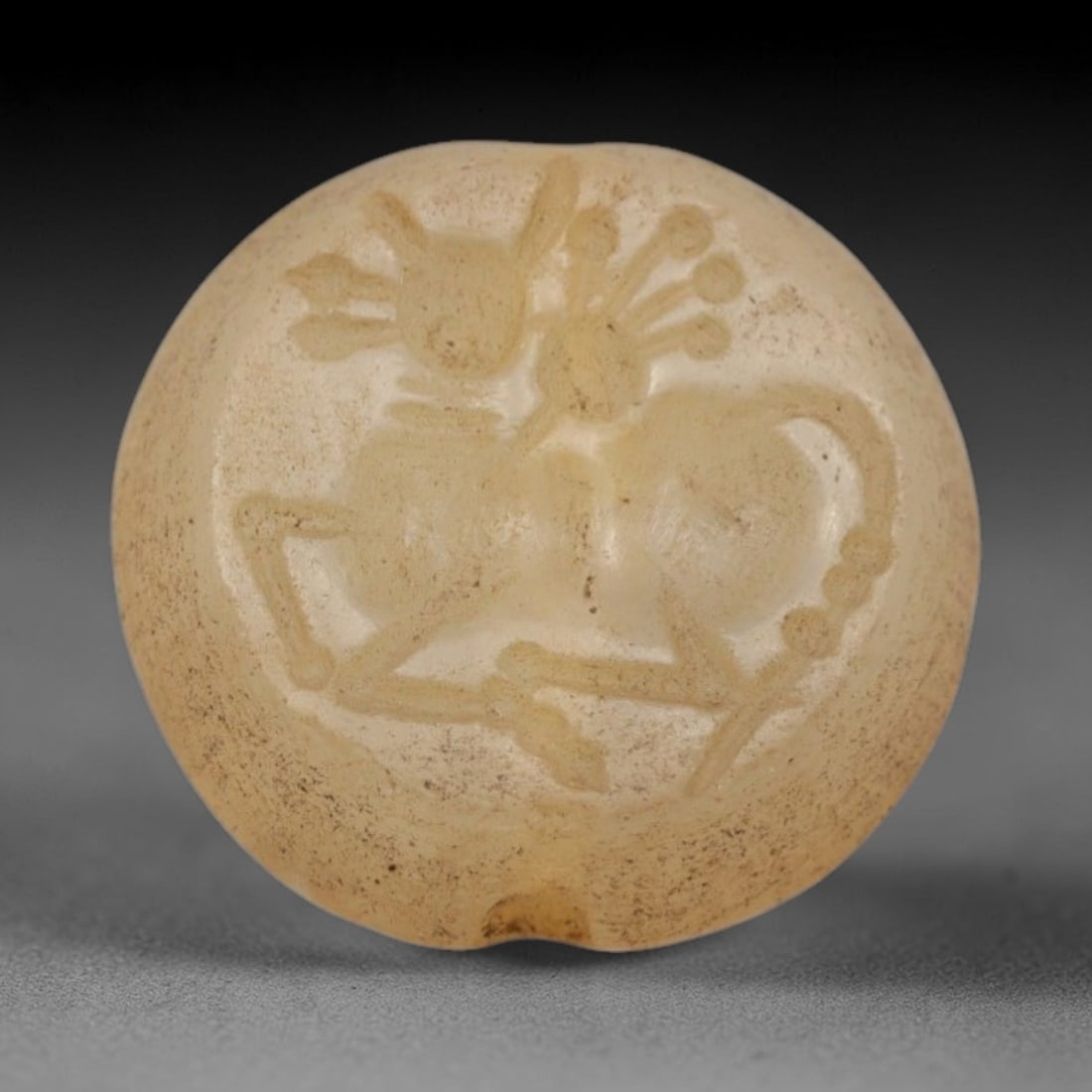 Ancient Rock Crystal Intaglio Bead - Near Eastern Animal Figure, 51ZS: Crafted from translucent rock crystal, this circular intaglio bead bears a deeply incised reclining animal figure, rendered with linear detailing to define its stylized antlers, segmented body, and cu