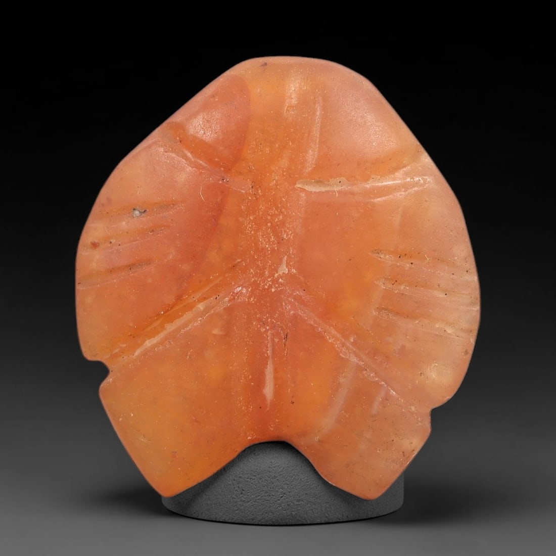 Ancient Carnelian Fish Amulet - Egyptian Figurine, 50XS: This amulet is carved from warm orange-red carnelian, shaped into a stylized fish form with incised linear detailing representing fins and anatomical segmentation across its surface. The compact, roun