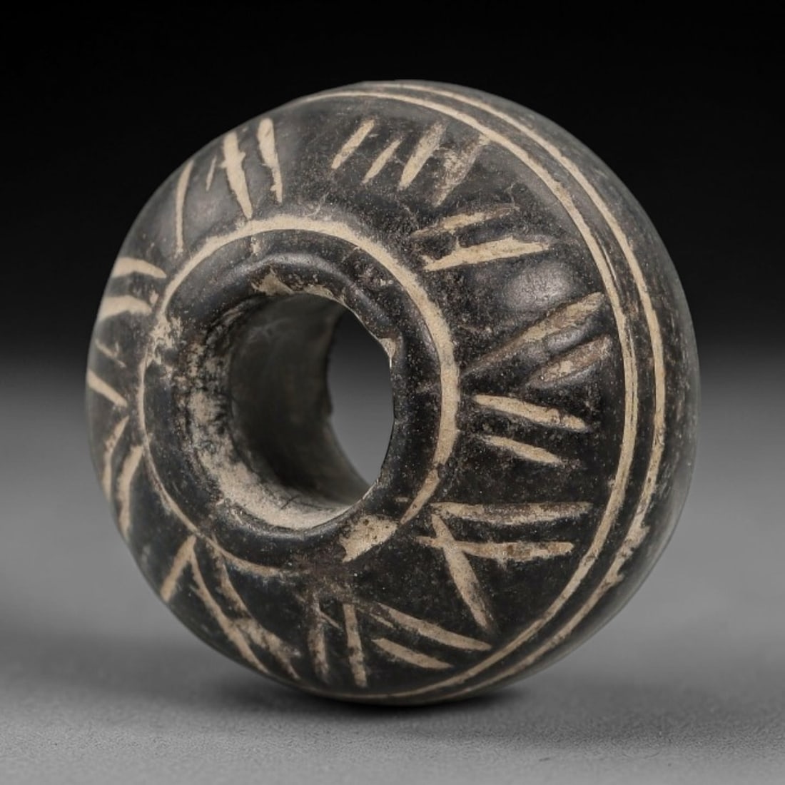 Ancient Bone Spindle Whorl - Near Eastern Crosshatched Motif, 1AJ: This ancient Near Eastern spindle whorl is carved from bone, featuring a biconvex form with a central perforation. The surface is decorated with incised crosshatched and circular motifs, a common deco