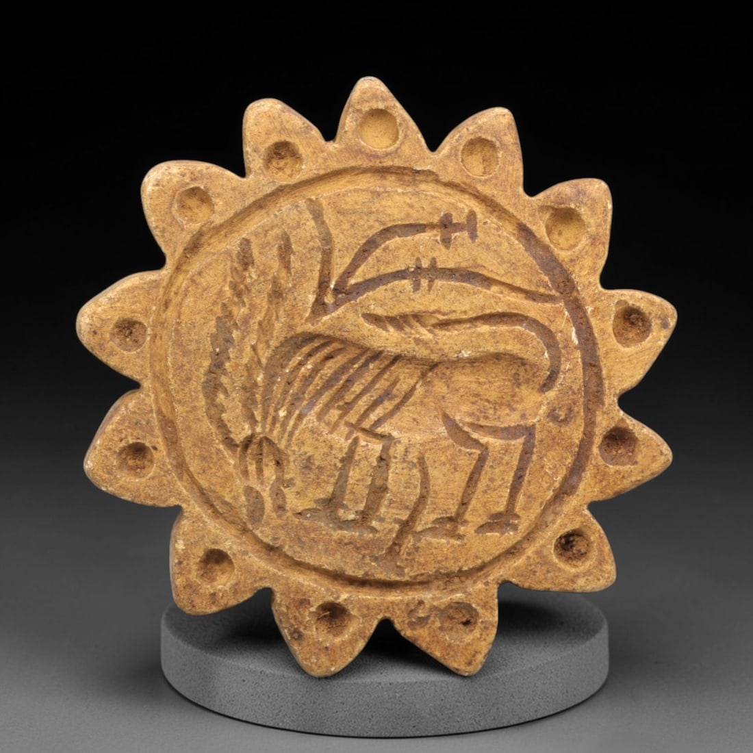 Ancient Steatite Ibex Stamp Seal - Near Eastern Sun Amulet, 82ZP: Carved from warm tan steatite, this circular stamp seal features a radiating sunburst border with evenly spaced perforations, enclosing a stylized ibex in incised relief. The ibex is rendered with pro