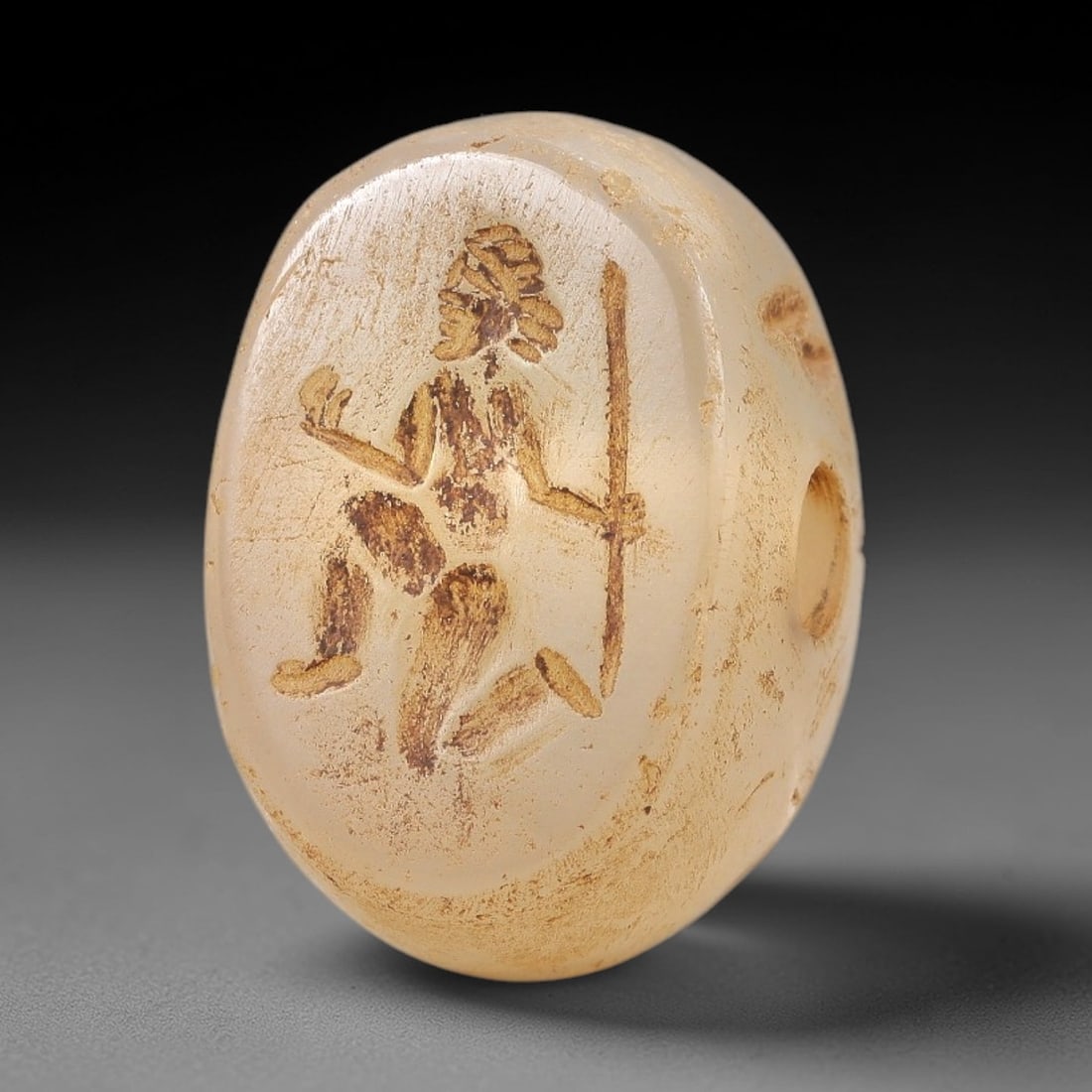 Ancient Near Eastern Chalcedony Hemispherical Stamp Seal - Warrior Figure Artifact, 19AN: This artifact is a hemispherical chalcedony stamp seal, executed in the classic glyptic tradition of the ancient Near East. The face features a kneeling warrior figure holding a spear and a circular o