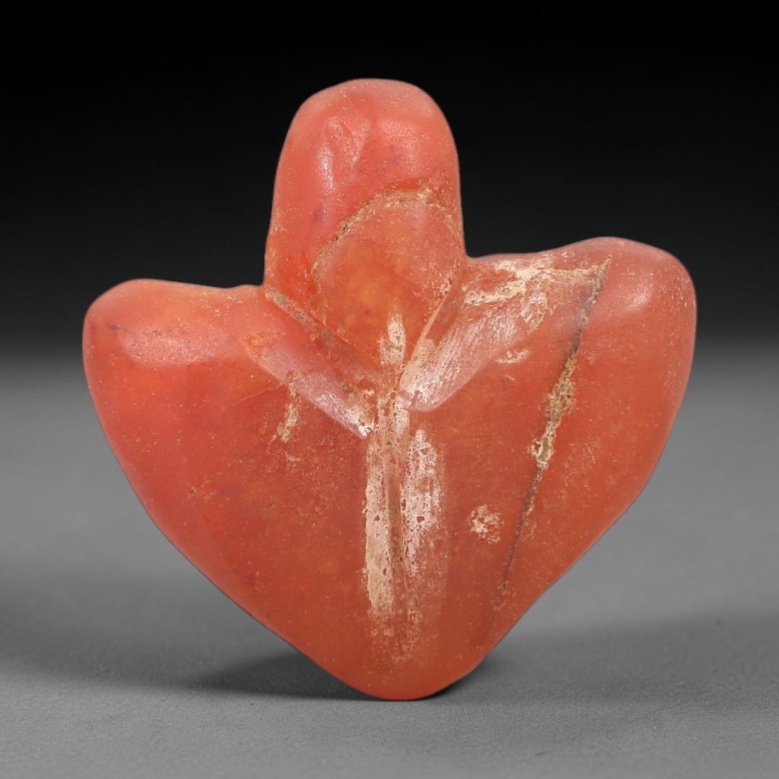 Ancient Agate Heart - Egyptian Amulet Figurine, 55XS: This amulet is carved from rich orange-red agate, exhibiting natural banding and a smooth, matte finish typical of ancient Egyptian glyptic craftsmanship. The form is a stylized heart, with rounded co