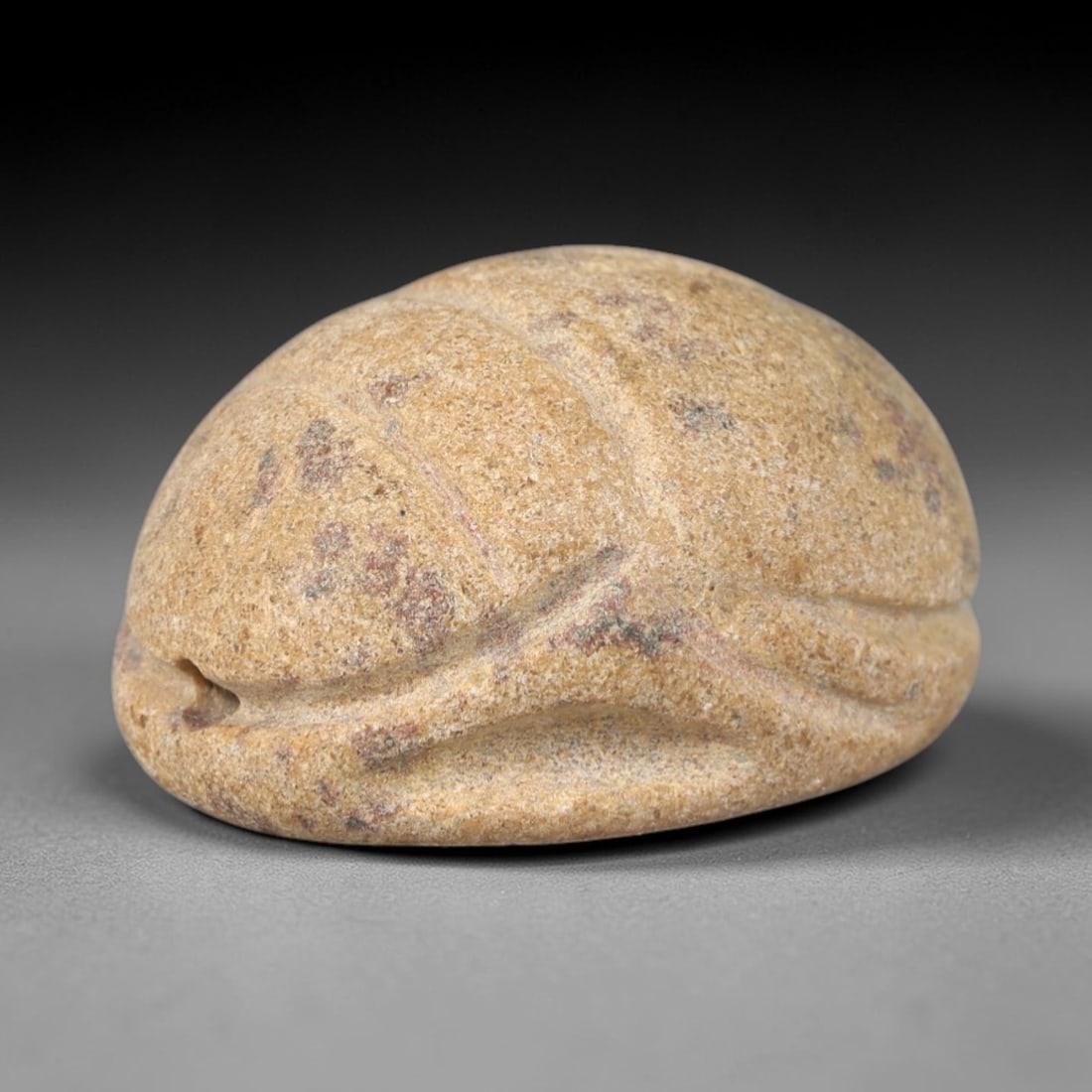 Ancient Sandstone Scarab Amulet - Egyptian Figurine, 97AP: This artifact is carved from light tan sandstone, exhibiting a granular, matte finish with natural reddish-brown mineral inclusions and subtle surface wear consistent with age. The form is a stylized