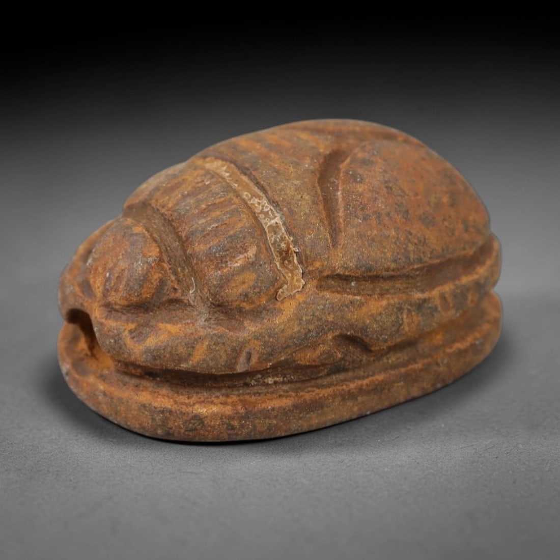 An Ancient Near Eastern Stone Scarab Stamp Seal, 1st Millennium BCE, 100AC: Carved from warm, earth-toned stone with natural surface patination and subtle tonal variation, the object is formed as an oval scarab seal. The dorsal side is modeled in low relief with a segmented c