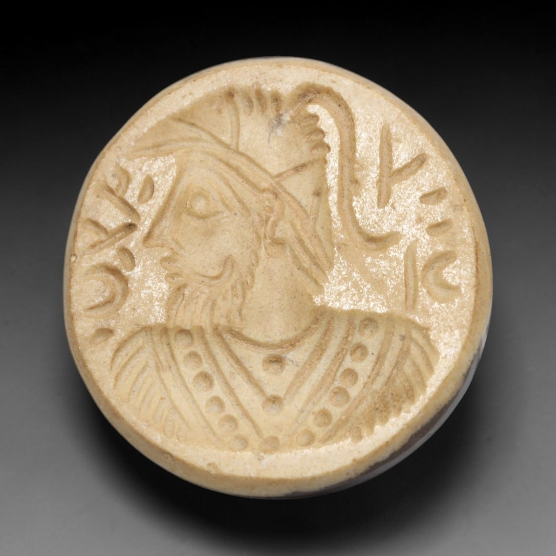 Ancient Agate Intaglio Bead - Near Eastern Figural Bust with Inscription, 30ZW: Carved from pale banded agate, this circular intaglio bead features a recessed profile depiction of a bearded figural bust adorned with a crested helmet and patterned attire, flanked by incised script