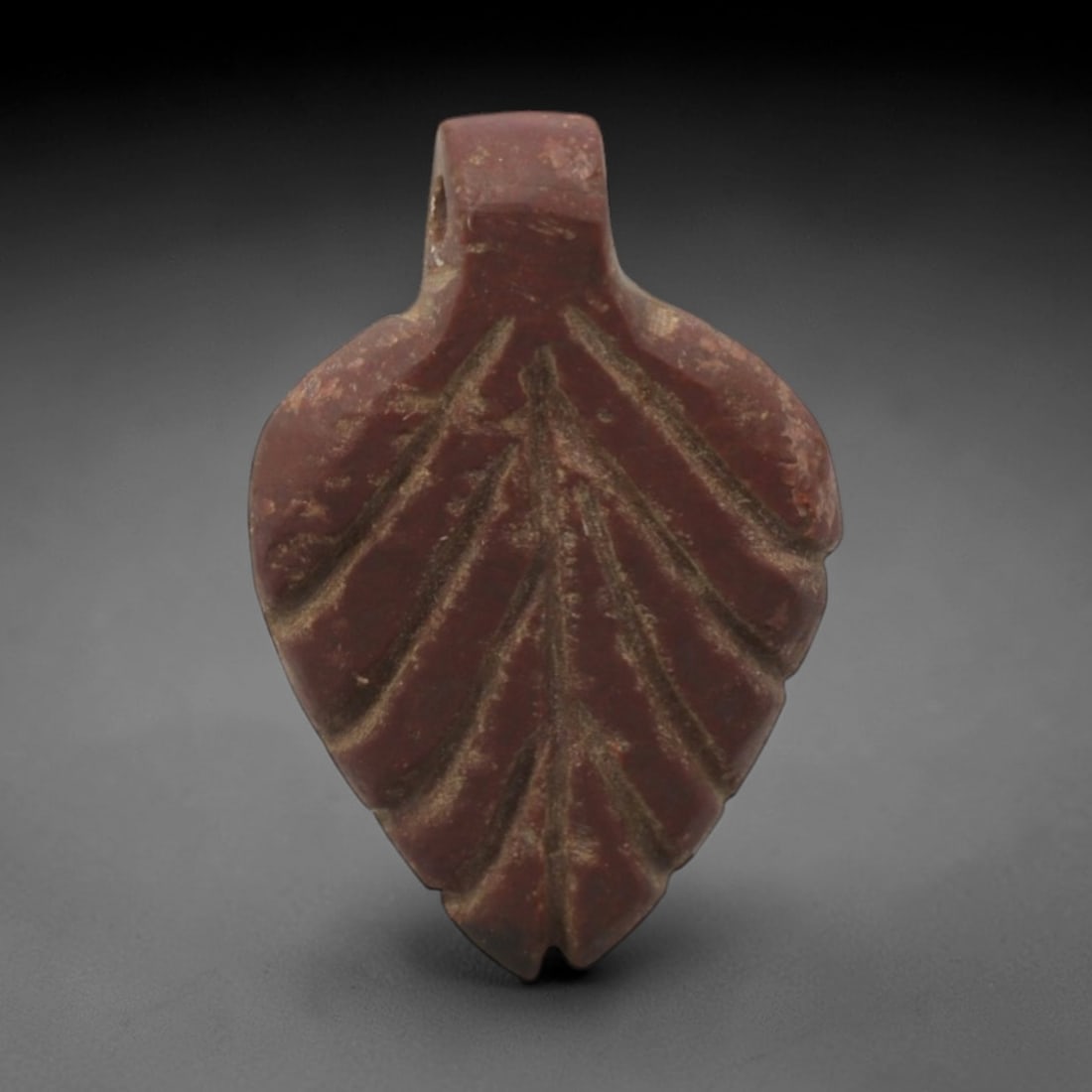 Ancient Stone Leaf - Near Eastern Amulet Pendant, 29XR: Carved from rich red stone, this amulet is shaped like a stylized leaf with incised veins and a rectangular suspension loop at the top. The botanical design is characteristic of Ancient Near Eastern v