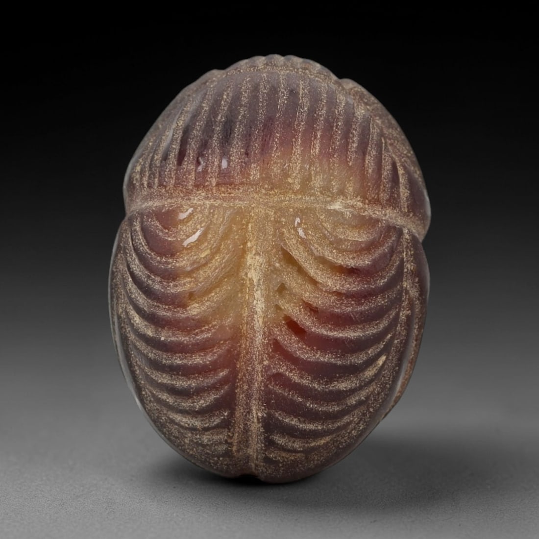 Ancient Banded Agate Scarab Amulet - Egyptian Figurine, 78AJ: Carved from rich banded agate with deep purple-red to amber gradients, this amulet is formed as a stylized scarab beetle with deeply incised, rhythmic linear detailing to define segmented wing cases a
