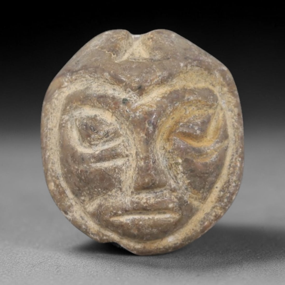 Ancient Stone Face Bead - Near Eastern Amulet, 71AP: Carved from compact stone, this face bead features a stylized anthropomorphic visage with incised eyes, nose, and mouth, framed by a raised circular border. The bead retains a small suspension hole at