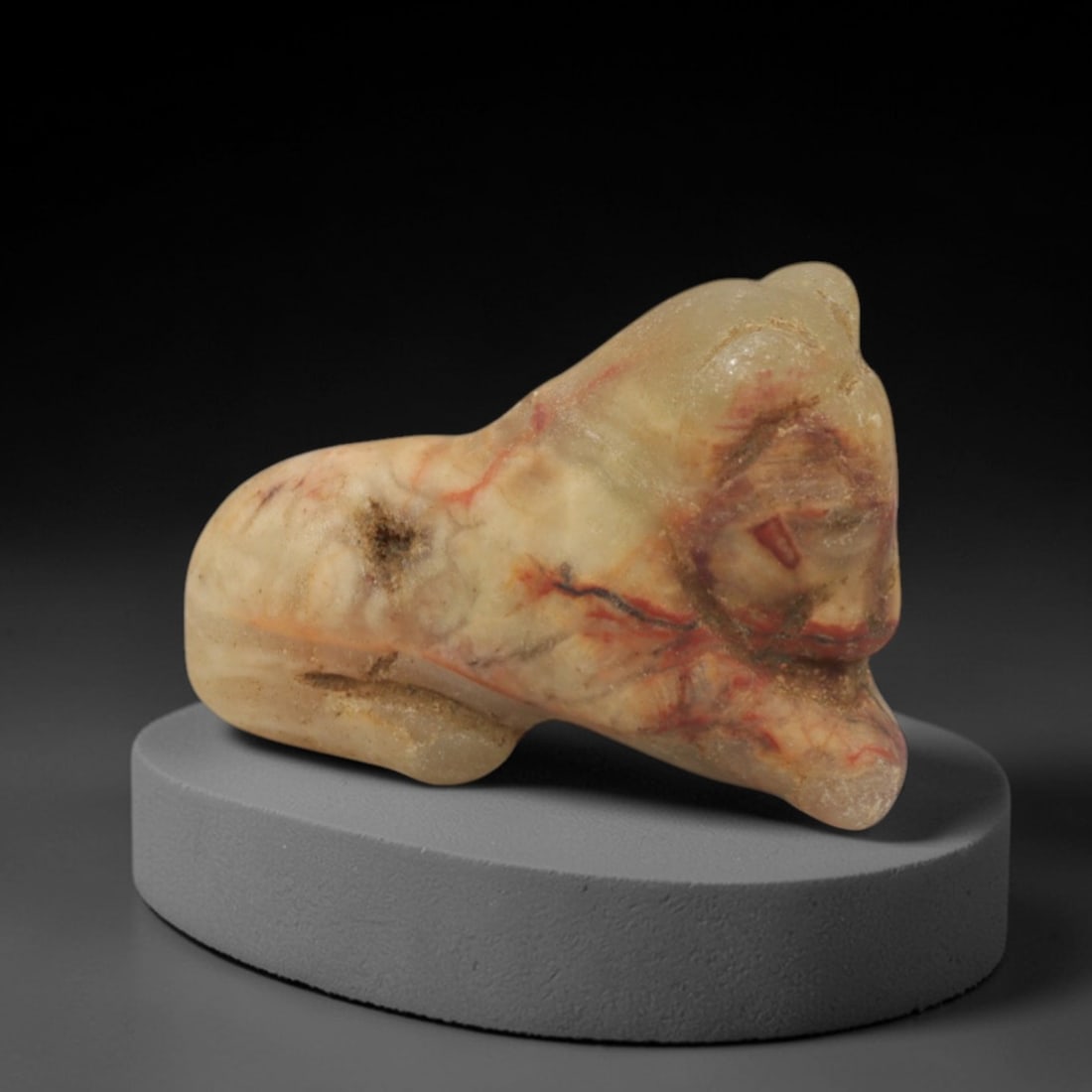 Ancient Cream Stone Recumbent Animal Amulet - Near Eastern Miniature Figurine, 5XQ: Carved from a creamy-tan stone with natural red and grey mineral banding, this charming amulet depicts a stylized recumbent animal, likely a bull or ram, a classic motif in ancient Near Eastern portab