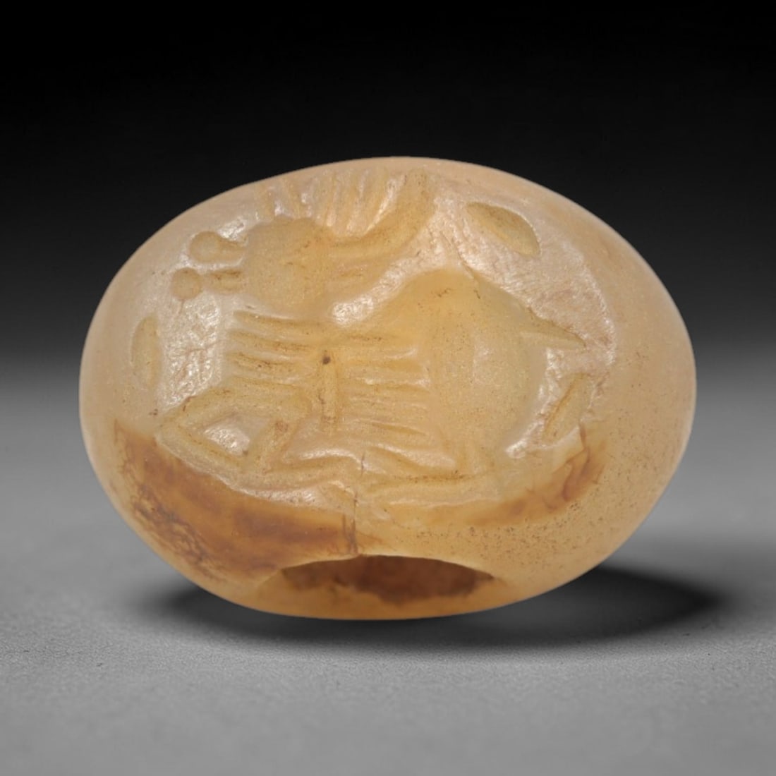 Ancient Chalcedony Stamp Seal - Near Eastern Caprid Figure, 56ZS: Crafted from translucent chalcedony, this oval stamp seal bears a deeply incised profile of a reclining caprid (ibex or goat), rendered with linear detailing to define its curved horns, ribcage, and l