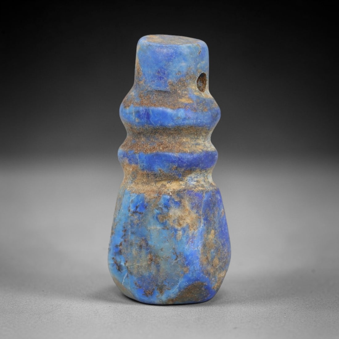 Ancient Lapis Lazuli Amulet - Egyptian Ritual Pendant, 25AP: Carved from lapis lazuli, this amulet features a stepped, segmented form with two raised horizontal bands encircling its upper body, a cylindrical top lug pierced for suspension, and a faceted lower b