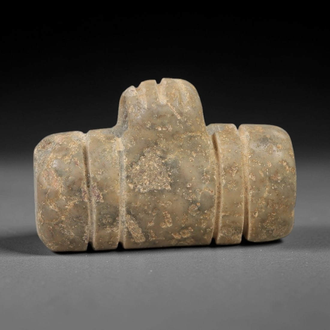 Ancient Stone Tyet Amulet - Egyptian Ritual Figurine, 85AG: This amulet is carved from a single piece of mottled grey-green stone, exhibiting a granular texture with subtle ochre patina and natural mineral inclusions across its surface. The form is a stylized
