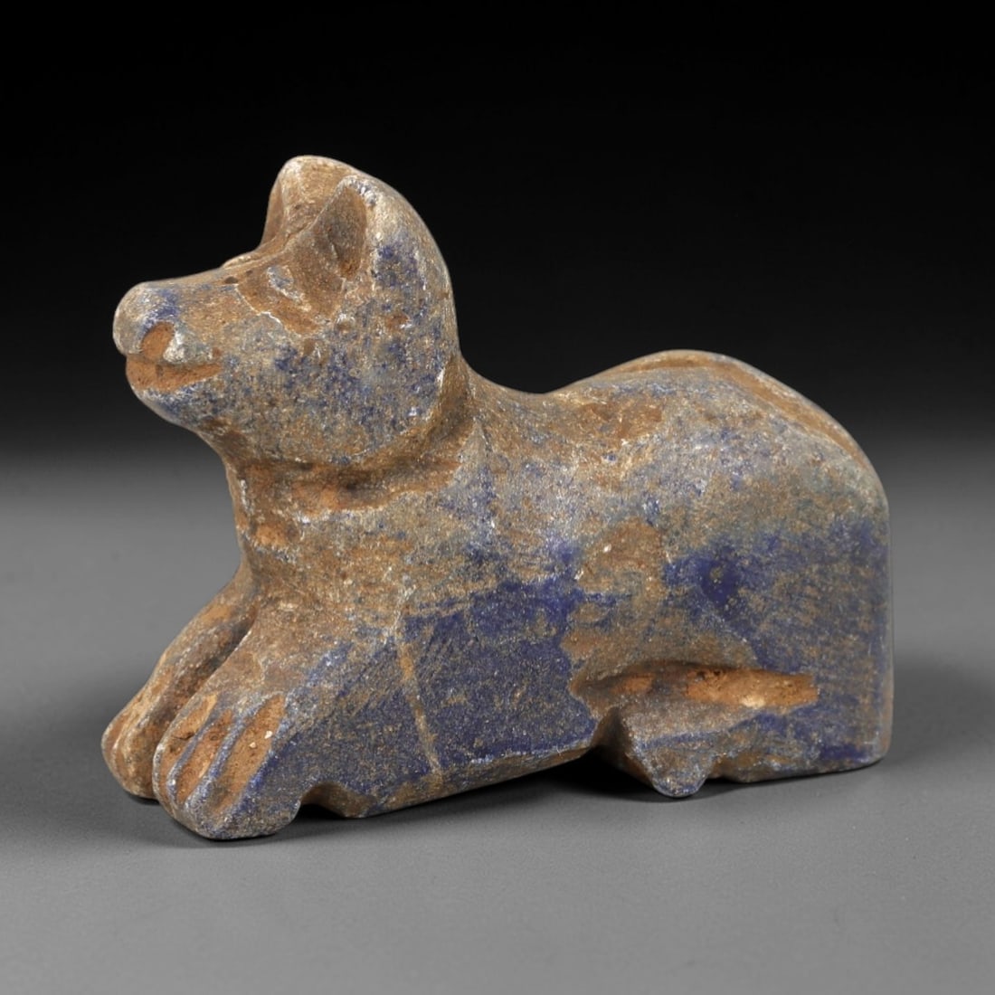 Ancient Lapis Lazuli Feline Effigy - Near Eastern Animal Figurine, 24AM: This feline effigy is carved from rich blue lapis lazuli with natural earthy inclusions, depicting a stylized cat or lion in a crouched, recumbent posture. The piece features incised linear detailing