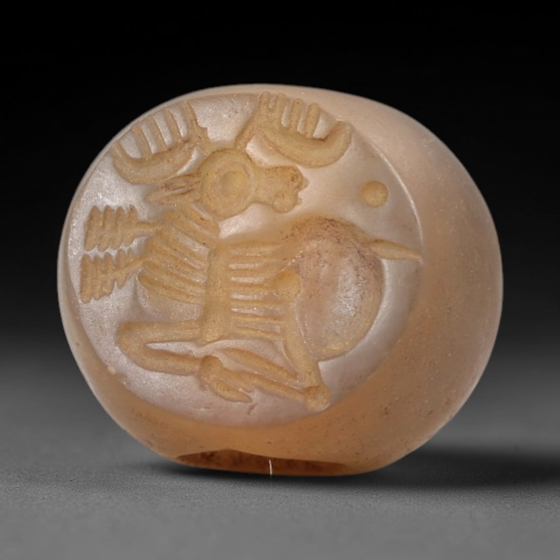 Ancient Chalcedony Stamp Seal - Near Eastern Stag Figure, 15AN: Carved from translucent pale chalcedony, this hemispherical stamp seal depicts a stylized stag with prominent curved antlers, linear incised details defining its skeletal structure and limbs, and a ci