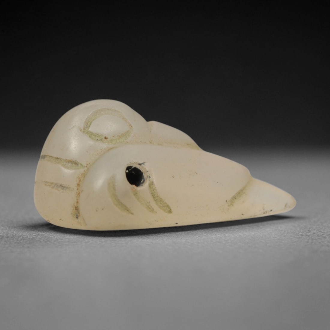 Ancient Opaque Glass Duck Amulet - Egyptian Animal Figure, 71ZW: This amulet is crafted from translucent pale ivory glass, shaped in the form of a stylized duck head with a pointed beak and rounded cranium. Incised lines filled with green pigment define the facial