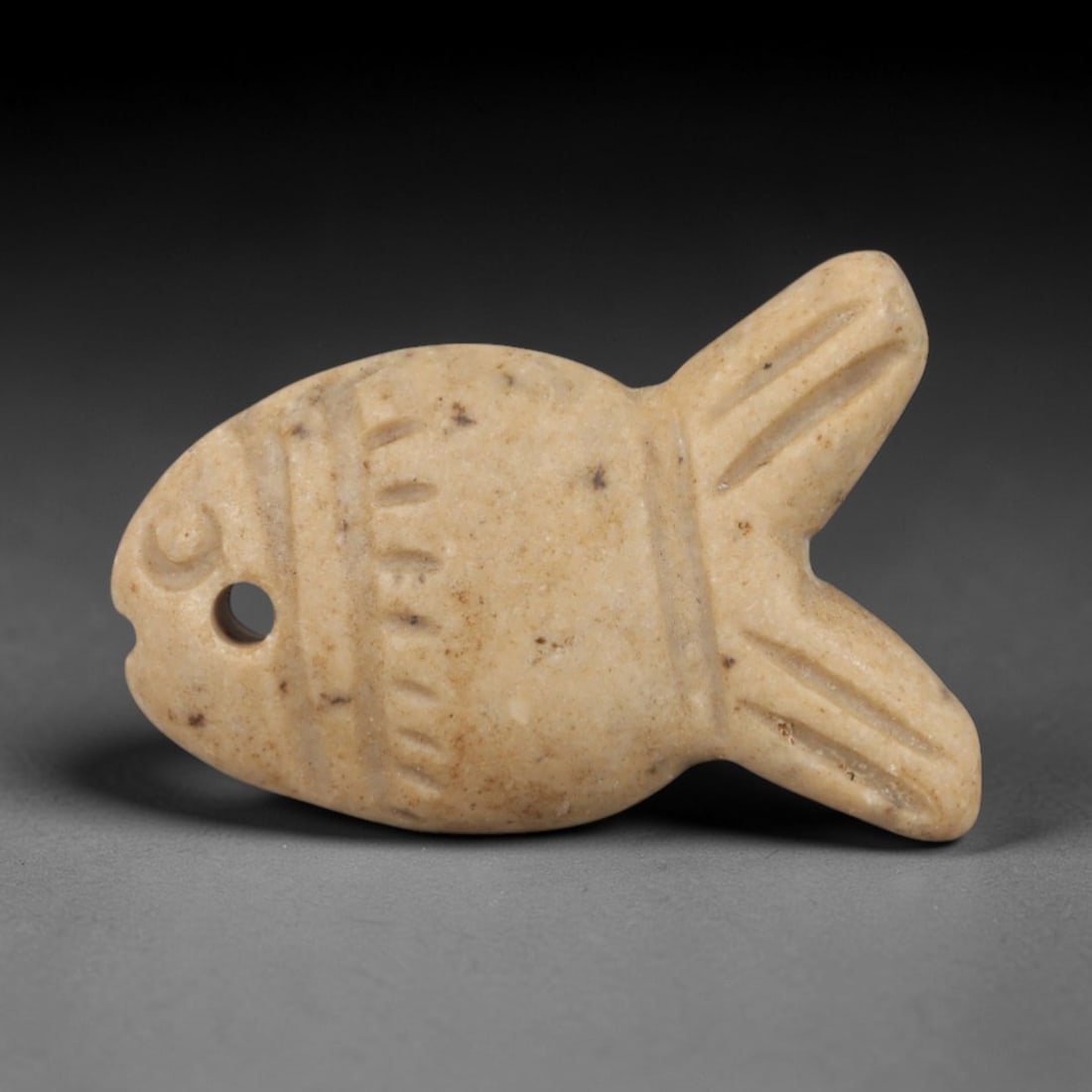Ancient Steatite Fish Amulet - Egyptian Ritual Pendant, 32AR: Carved from smooth steatite, this fish amulet follows the stylized form characteristic of ancient Egyptian protective iconography. The piece features incised linear details defining the body segments,