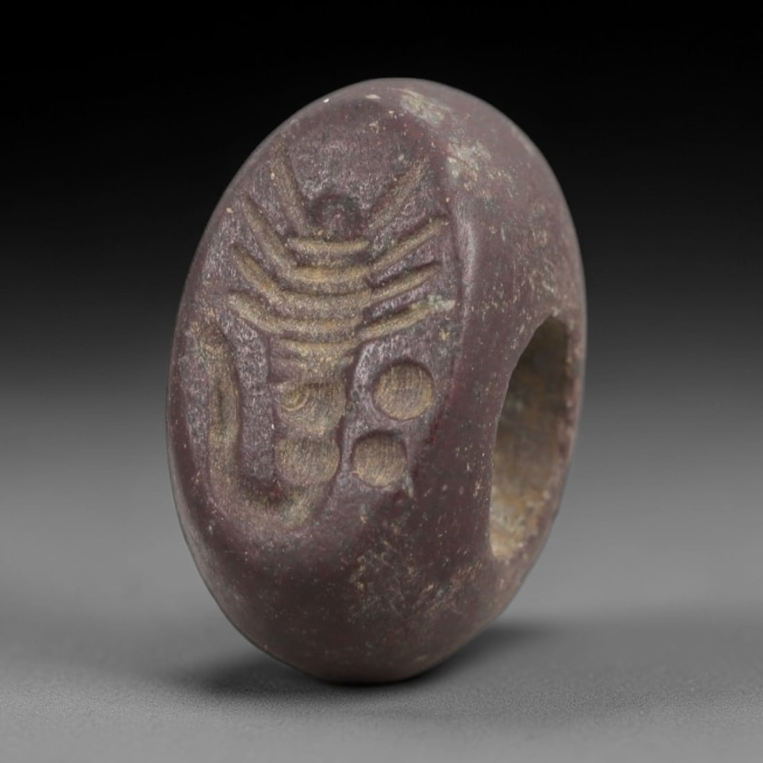 Ancient Red Stone Stamp Seal - Near Eastern Amulet, 16AN: Crafted from dense, reddish-purple stone, this hemispherical stamp seal bears an incised design featuring a stylized, radiating motif with layered linear elements, paired with circular dot symbols. Th