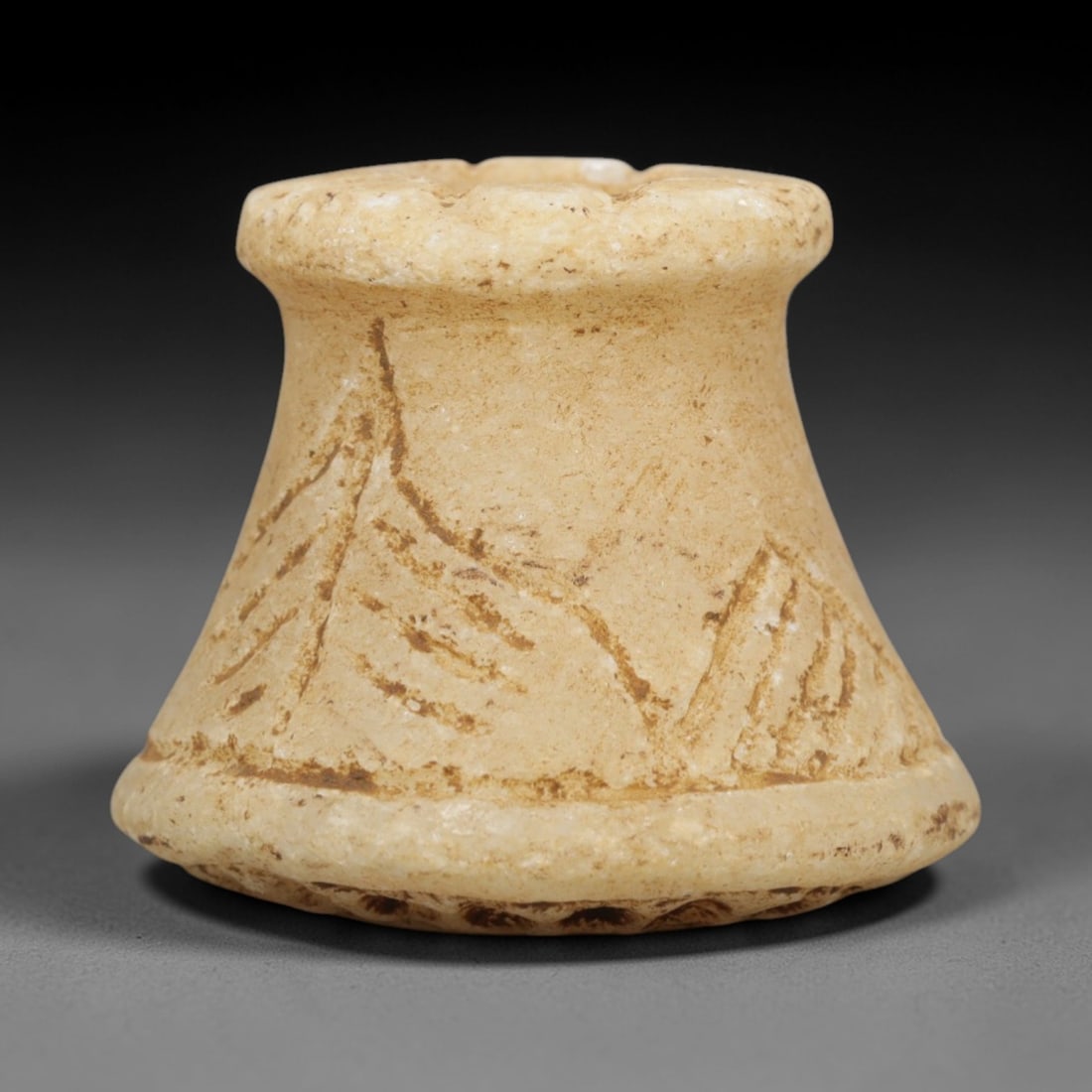 Ancient Stone Spindle Relic - Near Eastern Figurine, 80ZP: Carved from pale tan limestone, this flared spindle-shaped relic features incised vegetal motifs across its conical body, with a scalloped lower edge and a central perforation through its wider end, c