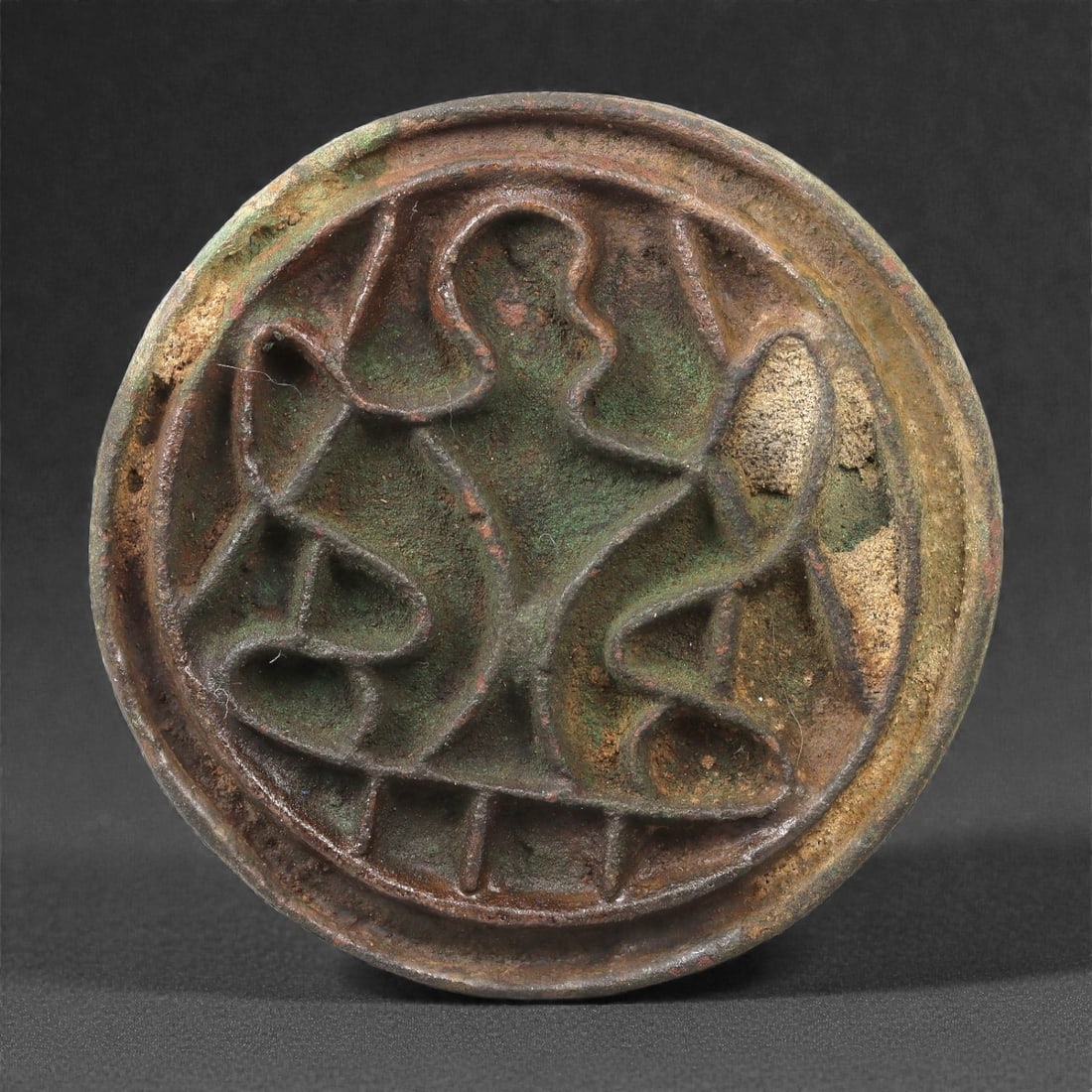 A Kushano-Bactrian Bronze Stamp Seal with Anthropomorphic Motif, 2nd-4th Century CE, 59LP: Cast in bronze, the circular stamp seal bears a recessed linear design forming an abstract anthropomorphic figure with outstretched, looping arms. The body is indicated through continuous raised conto