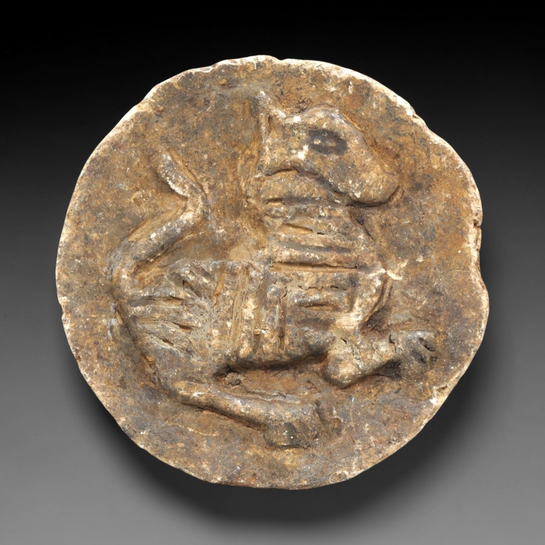 Ancient Stone Plaque Relief - Near Eastern Lion Figurine, 84ZP: Carved from weathered stone, this circular plaque features a striding lion in high relief, with incised lines defining its striped pelt, facial features, and curled tail. The lion is depicted in a dyn