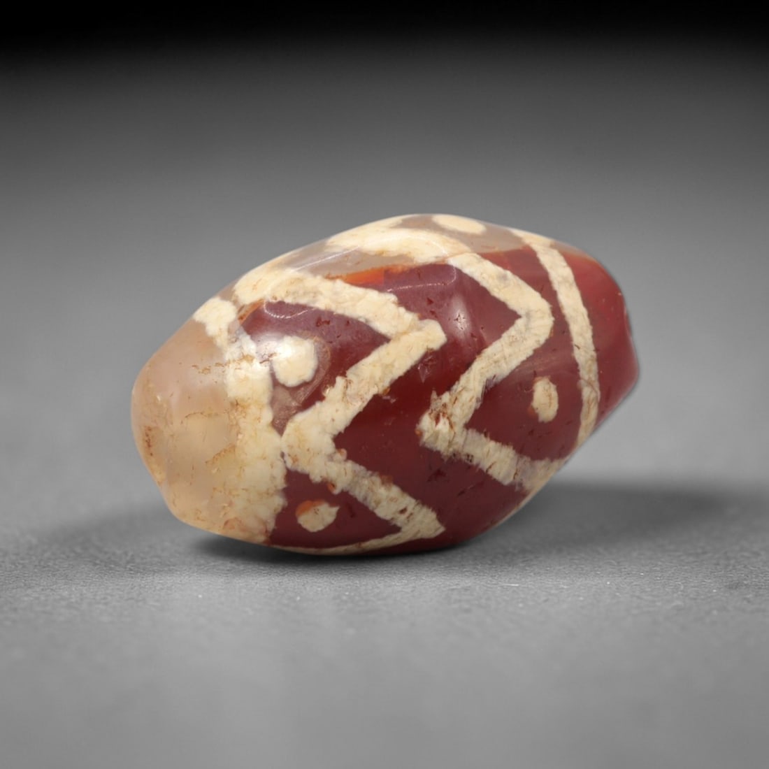Ancient Carnelian Geometric Dzi Bead - Himalayan Amulet, 77XV: Crafted from rich translucent carnelian, this compact ovoid bead features bold etched white geometric zigzag lines and circular dot accents, executed in traditional Himalayan Dzi bead techniques. The