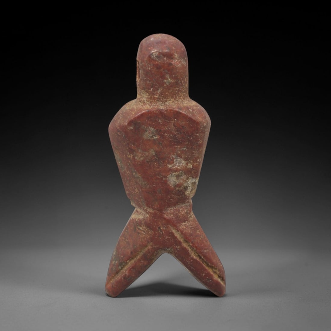 Ancient Stone Anthropomorphic Amulet - Near Eastern Figurine, 59XQ: This amulet is carved from a rich, reddish stone, shaped into an abstract anthropomorphic form with a rounded head, narrow torso, and bifurcated lower section, lacking perforations and suggesting a vo