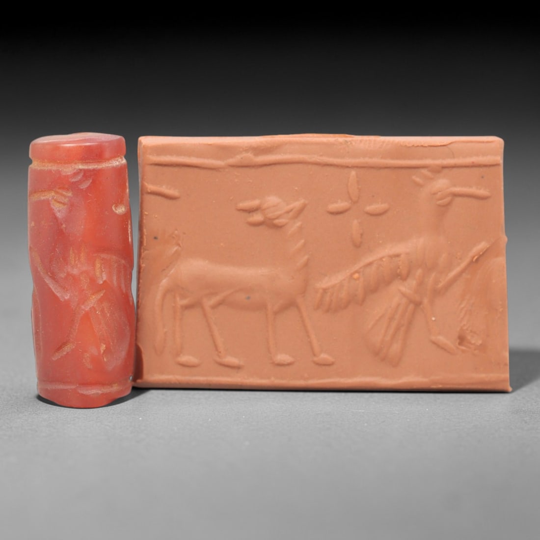 Ancient Carnelian Cylinder Seal - Mesopotamian Stag & Avian Scene, 74ZS: Carved from rich red carnelian, this ancient Mesopotamian cylinder seal features a refined linear relief composition of a standing stag and a large winged bird, separated by a floral cross symbol, exe